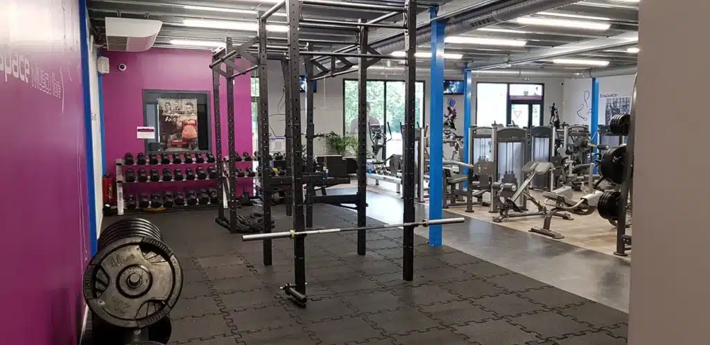 Salle de sport moderne avec espace musculation ('Espace Muscu'), rack d'entraînement, haltères, et machines de cardio et de renforcement.