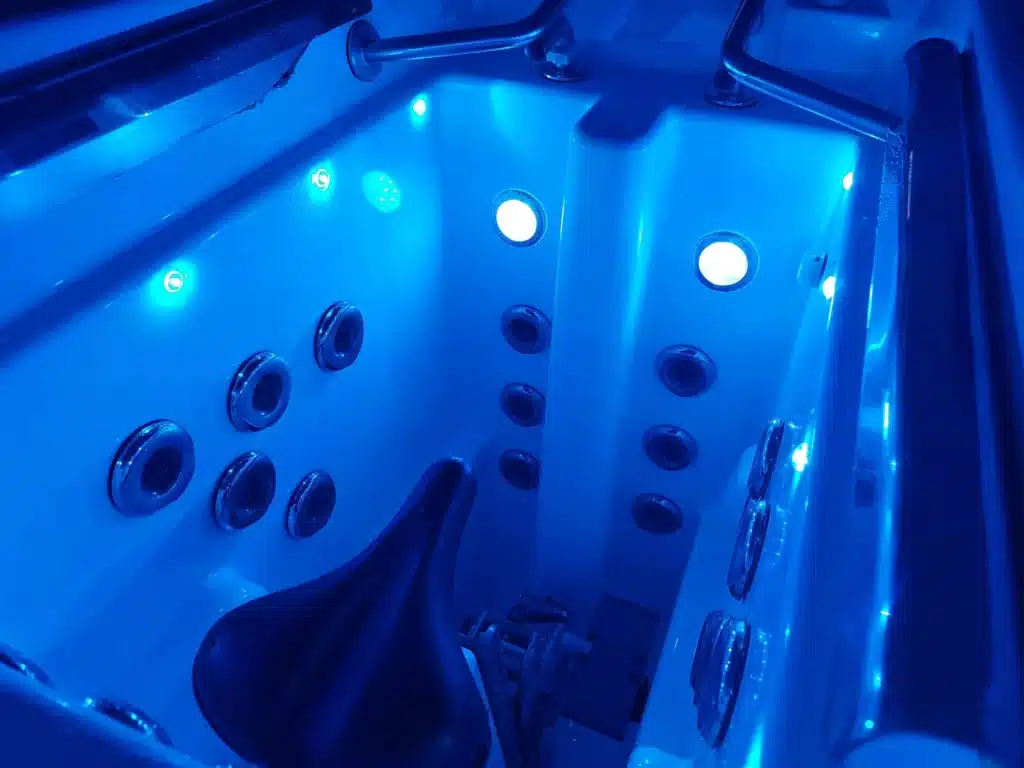 Intérieur bleu lumineux d'un spa de nage avec jets de massage, vélo aquatique intégré et barres de maintien. Idéal pour l'hydrothérapie.