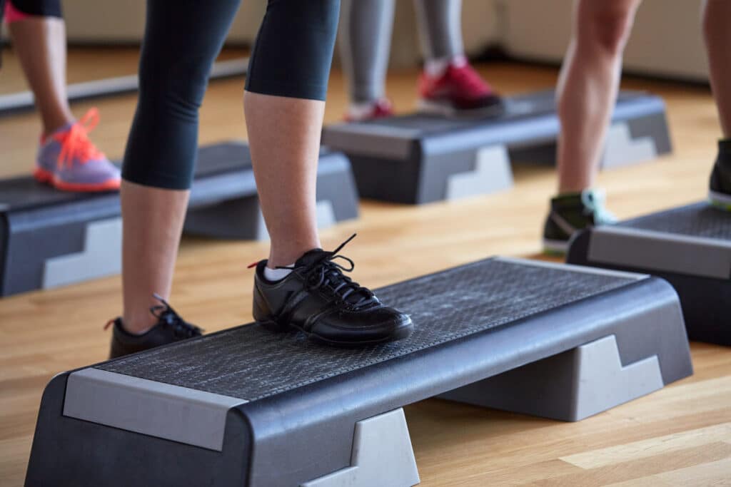 Plusieurs personnes faisant de l'aérobic sur des plateformes de step noires, montrant leurs jambes et chaussures de sport.